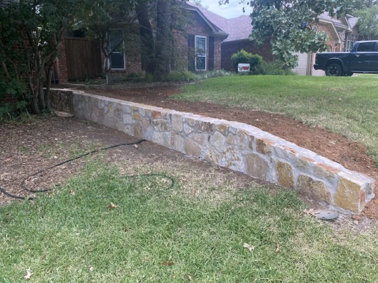 Newly built Milsap stone retaining wall in front yard of DFW brick home, replacing old wood cross-tie wall on clay soil
