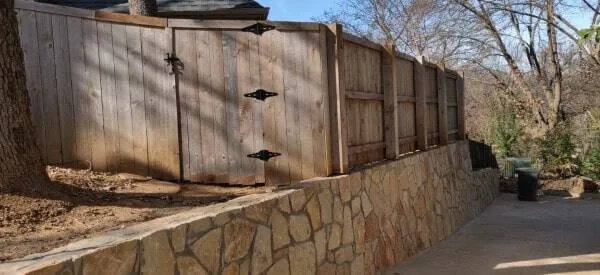 Natural stone retaining wall supporting a wood privacy fence along a residential property in Grapevine, TX