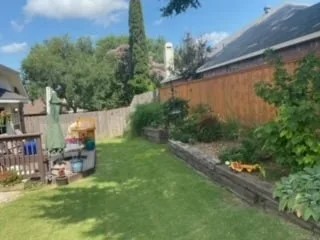 Completed railroad-tie retaining wall replacement with lush green lawn and tiered garden beds in a Dallas backyard
