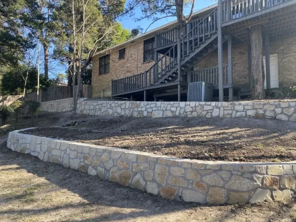 Two-tier Granbury stone retaining wall on a sloped backyard behind a two-story brick home in Dallas, TX
