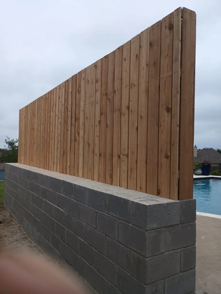 New concrete block retaining wall with cedar fence on top beside a residential pool in the Dallas–Fort Worth area