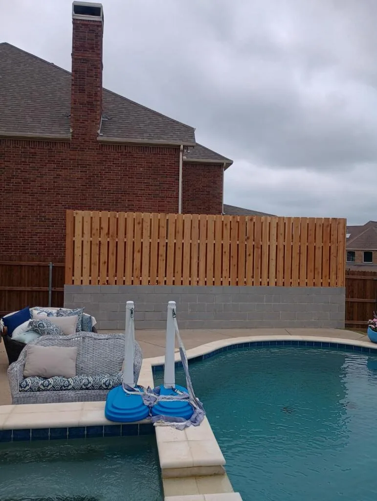 Concrete Block Wall & Cedar Fence Installation | JCL Colleyville New concrete block retaining wall with cedar privacy fence on top beside a residential pool in DFW backyard