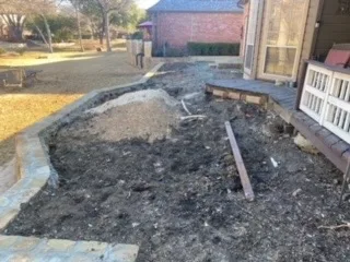 Excavated yard in DFW showing demolished railroad cross-tie retaining wall with exposed soil and gravel, ready for Milsap stone wall and patio installation