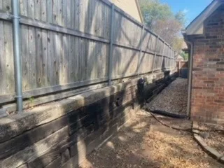 Failing Cross Tie Retaining Wall Before Replacement – Colleyville TX Deteriorating railroad cross tie retaining wall along wood privacy fence in DFW backyard, showing moisture damage and rot before Milsap stone replacement