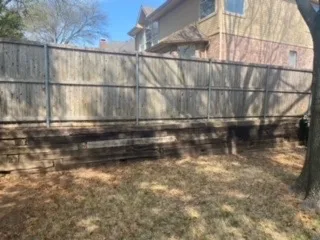 Failing Railroad Tie Retaining Wall Replacement – Colleyville TX Deteriorating railroad tie retaining wall with dark rotting timbers along fence line at DFW residential property awaiting replacement