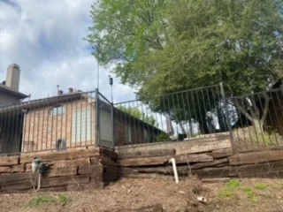 Failing Railroad Tie Retaining Wall Replacement Colleyville TX Failing railroad tie retaining wall with rotting timber layers along residential backyard slope in DFW, awaiting replacement with Milsap stone wall.