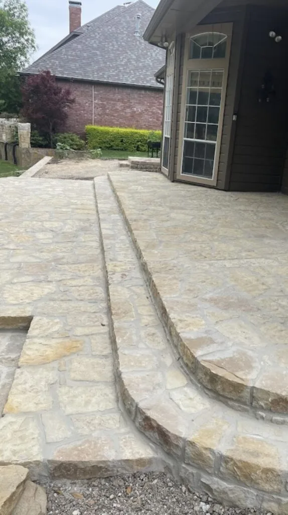 Curved Granbury or Milsap stone patio steps and landing beside a DFW home, part of a cross-tie wall replacement and patio addition project