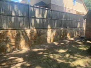 Milsap Stone Retaining Wall Replaces Cross Tie Wall | Colleyville Completed Milsap stone retaining wall replacing a deteriorating cross tie wall, topped with a wood privacy fence in a DFW backyard