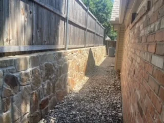 Completed Milsap stone retaining wall replacing old railroad cross-tie wall along narrow side yard with wood privacy fence, Colleyville TX
