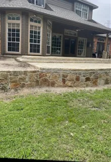 Completed Milsap stone retaining wall replacing old cross-tie wall, with new concrete patio steps at brick home in DFW
