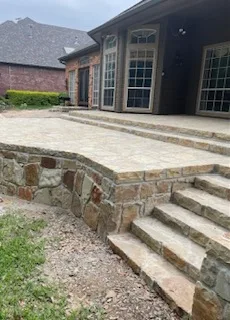 Milsap stone retaining wall with curved corner and matching stone steps leading to a new paver patio at a brick home in DFW