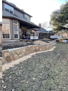 New Milsap stone retaining wall replacing old cross-tie wall along backyard of brick home, fresh-graded lawn, DFW area
