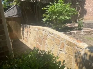Milsap Stone Retaining Wall Replacing Cross-Tie Wall | DFW Curved Milsap stone retaining wall replacing a railroad cross-tie wall, set between brick home and wood fence in DFW backyard