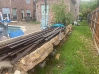 Railroad-Tie Wall Removal & Replacement – Colleyville TX Demolished railroad-tie retaining wall with old timber planks stacked on stone rubble beside a backyard pool in DFW, mid-demolition