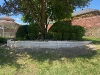 Curved concrete block retaining wall surrounding a tree and shrubs in a residential yard in Fort Worth, TX