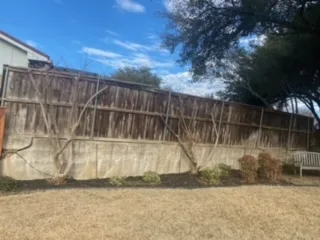 Old Concrete Retaining Wall Before Replacement – Irving TX Aging concrete retaining wall with weathered wood fence above it in Irving TX yard, before Milsap stone replacement by JCL Landscape Services