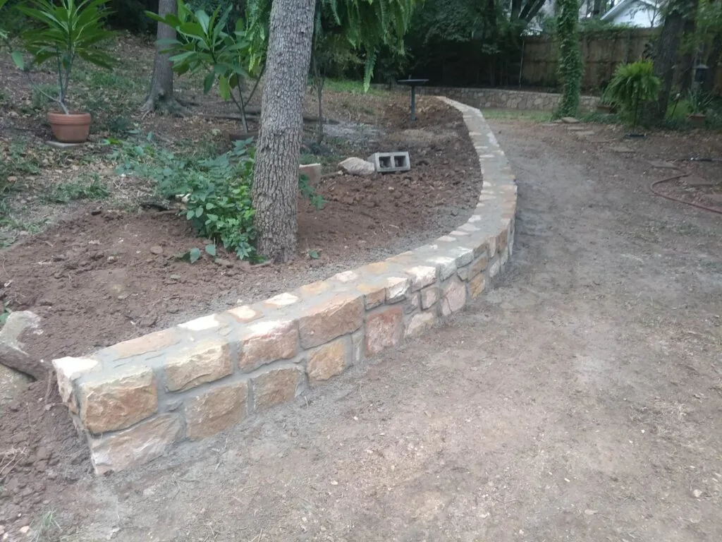 Curved Milsap stone retaining wall newly built in a residential backyard in Arlington, TX, replacing an old failing wall