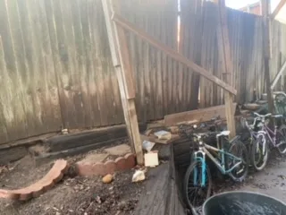 Deteriorating railroad cross tie retaining wall with rotted timbers and leaning wood fence in Grapevine TX backyard, before Milsap stone replacement