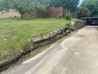 Failing Railroad-Tie Retaining Wall Replacement – Irving TX Deteriorating railroad-tie retaining wall along a residential driveway in Irving, TX, leaning and failing before Milsap stone replacement