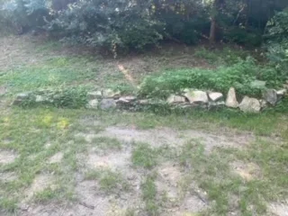 Deteriorating stone retaining wall with collapsed sections and overgrown vegetation in Arlington TX yard, awaiting Milsap stone replacement by JCL Landscaping.