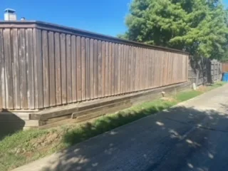 Failing Timber Retaining Wall Before Milsap Stone Replace – Lewisville Aging railroad-tie timber retaining wall supporting a tall wood fence along a residential driveway in Lewisville TX, showing deterioration before Milsap stone replacement