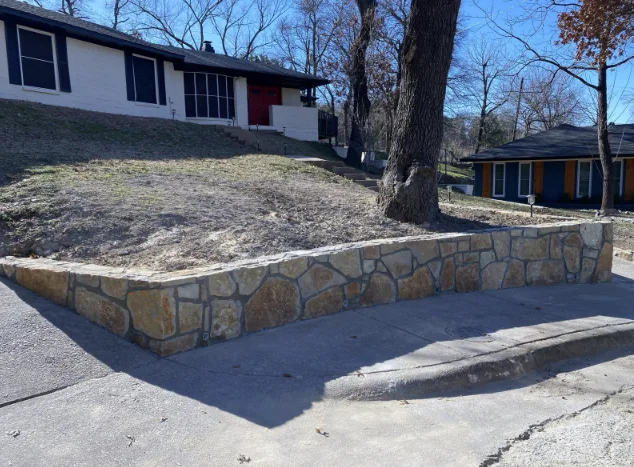 New Milsap stone retaining wall along residential street in Dallas TX, holding sloped front yard with mid-century home behind it