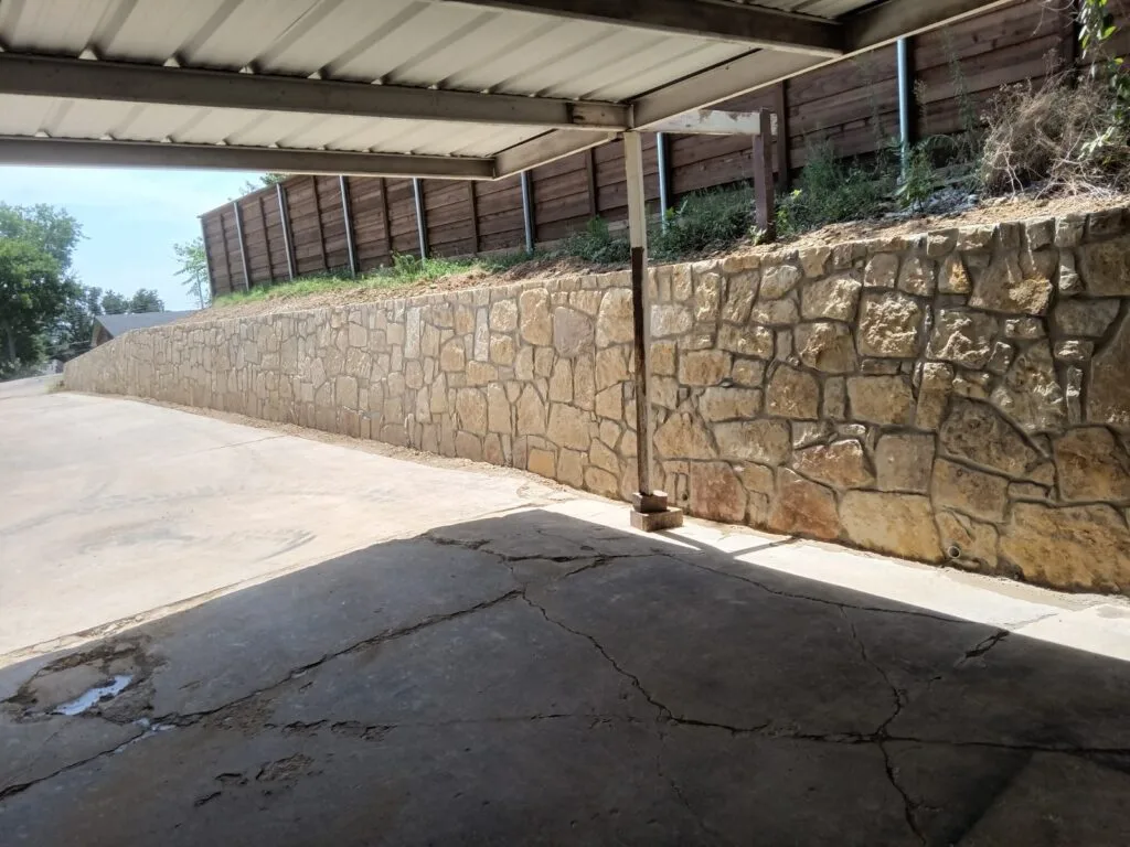 Milsap stone retaining wall along a residential driveway in Irving TX, replacing an old concrete wall, with a wooden fence on the slope above