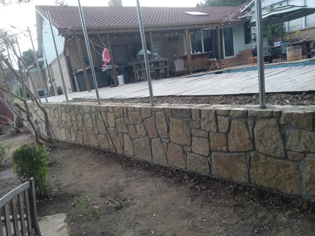 Milsap Stone Retaining Wall Replacement | Irving TX Newly built Milsap stone retaining wall supporting a wood deck and pool area at a residential backyard in Irving, TX