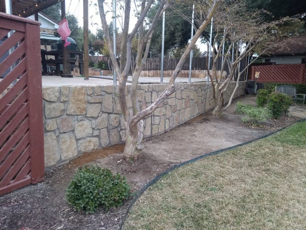 Completed Milsap stone retaining wall in Irving TX backyard, raising patio level with crape myrtle trees growing through wall base