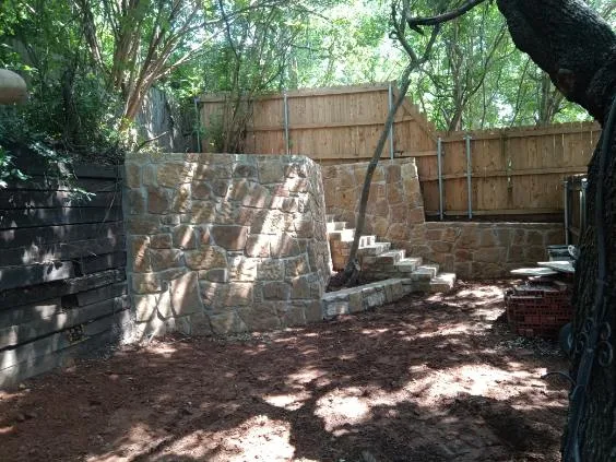 New Milsap stone retaining wall with integrated stone staircase replacing old cross tie wall in a wooded Colleyville backyard