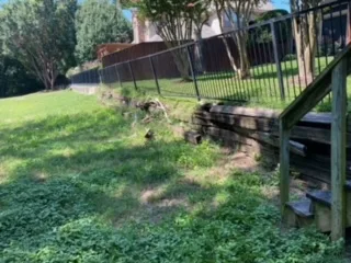 Deteriorating railroad cross tie retaining wall with overgrown vegetation along a sloped backyard in Coppell TX, before Milsap stone replacement