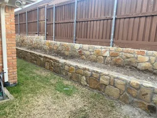 Two-tier Milsap stone retaining wall replacing a failed railroad tie wall along a wood privacy fence in Dallas, TX backyard