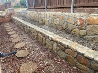 2-Tier Milsap Stone Retaining Wall Replacement | Dallas TX Two-tier Milsap stone retaining wall replacing old railroad tie wall, with stepping stone path, in a Dallas TX backyard