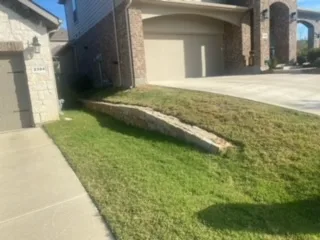 Failing railroad cross-tie retaining wall along a brick home's front yard in DFW, showing deteriorating timber before Milsap stone replacement