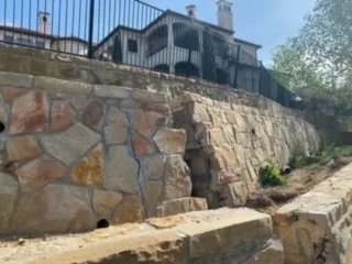Deteriorating natural stone retaining wall being demoed at a Dallas-area residential property before replacement with a poured concrete wall