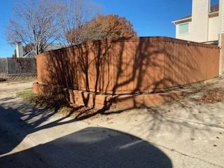 Deteriorating wood retaining wall with rusted brown timber boards leaning and failing along a residential sidewalk in DFW, ready for replacement