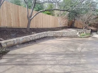 Newly built curved Milsap stone retaining wall replacing old railroad ties along a wood fence in a DFW backyard