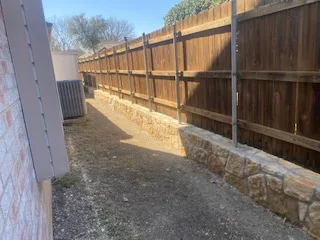 Completed Milsap stone retaining wall running along wooden privacy fence, replacing old railroad tie wall in DFW residential backyard