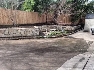 Completed Milsap stone retaining wall replacing old railroad ties, with tiered planting bed along wood fence in Dallas–Fort Worth backyard