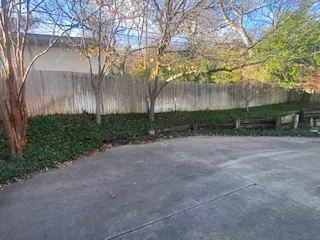 Flat concrete patio and wood privacy fence where a failing railroad tie retaining wall will be replaced with Milsap stone in Dallas, TX