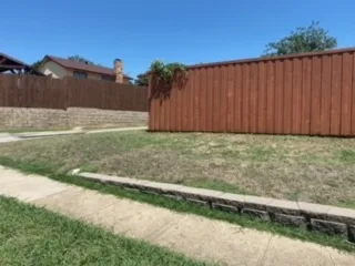 Milsap Stone Retaining Wall Replacement – Carrollton TX Low stone retaining wall along residential yard edge after replacement with Milsap stone, Carrollton TX, with wood privacy fence behind