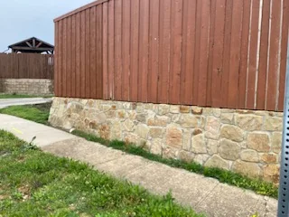 Milsap stone retaining wall base supporting a wood fence panel along a concrete sidewalk in Carrollton TX