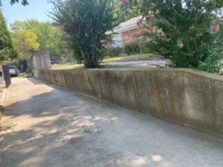 Aging concrete retaining wall with rust stains along residential driveway in Arlington TX before Milsap stone replacement