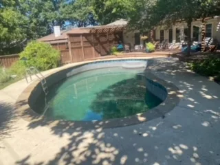 Older in-ground swimming pool with green water and concrete surround in a Dallas backyard, a candidate for partial pool demolition