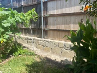Completed Milsap stone retaining wall along wood privacy fence in Dallas backyard, replacing deteriorating concrete wall