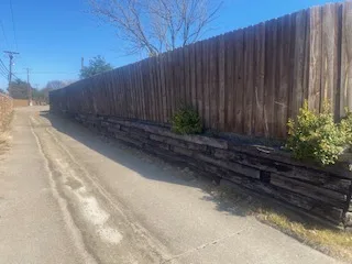 Railroad Tie Retaining Wall Before Replacement — Plano TX Deteriorating railroad tie retaining wall along a residential alley in Plano TX, showing aged dark timber blocks before natural stone replacement