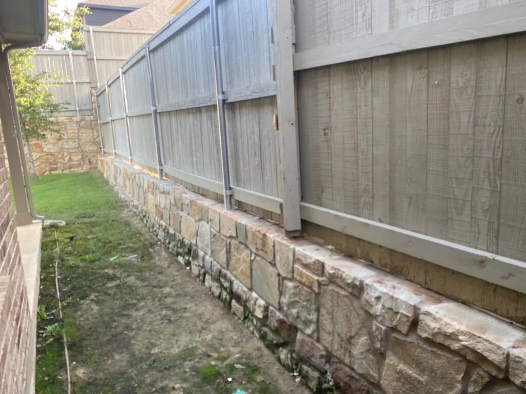 Completed Milsap stone retaining wall running along wooden privacy fence in DFW residential backyard, leveling yard grade