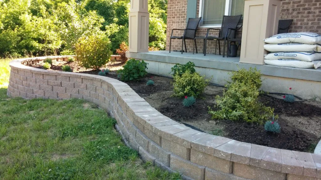 Curved concrete block retaining wall bordering a raised front-yard planting bed beside a brick home patio in the Dallas–Fort Worth area