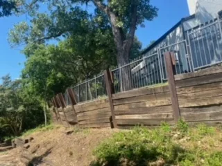 Failing Cross-Tie Retaining Wall Replacement | Irving TX Aging railroad cross-tie retaining wall with vertical timber posts leaning and deteriorating along a residential slope in Irving, TX, awaiting replacement