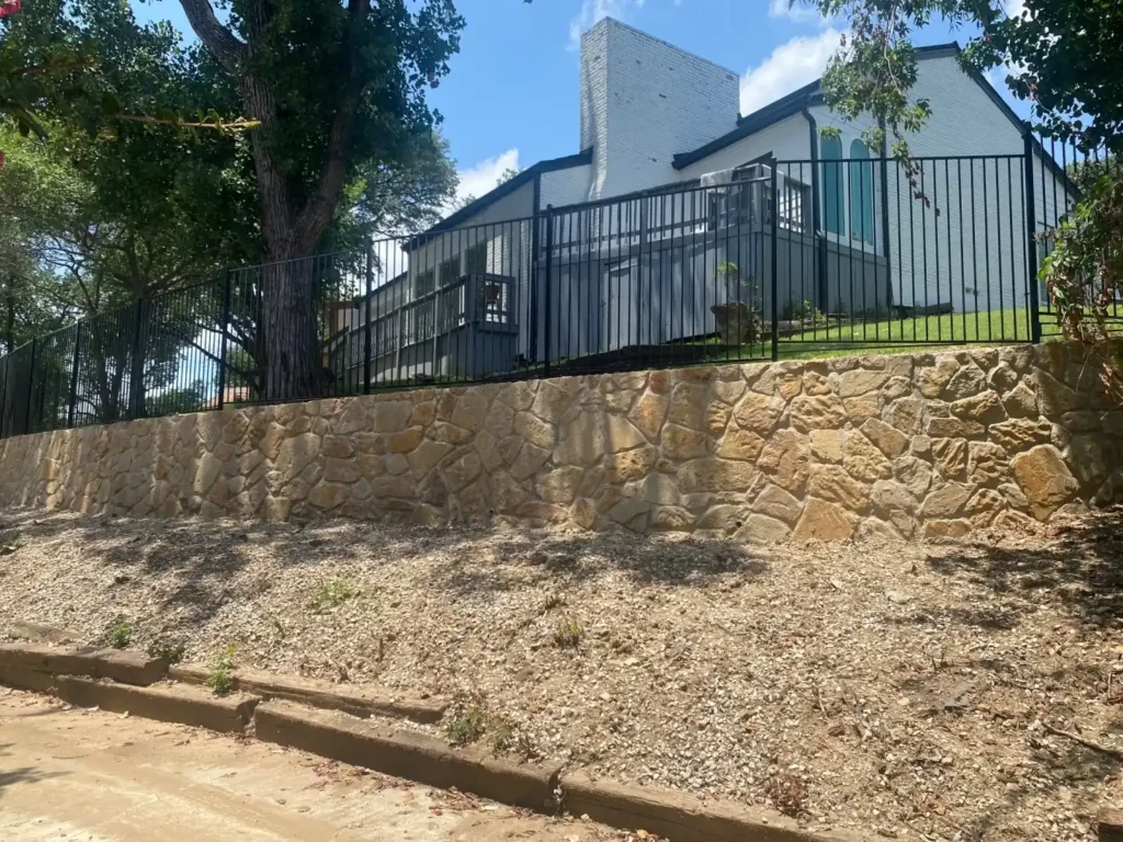 Milsap Stone Retaining Wall Replaces Cross Ties | Irving TX Completed Milsap stone retaining wall replacing deteriorated cross-tie wall at Irving TX home, with black iron fence and stairway above
